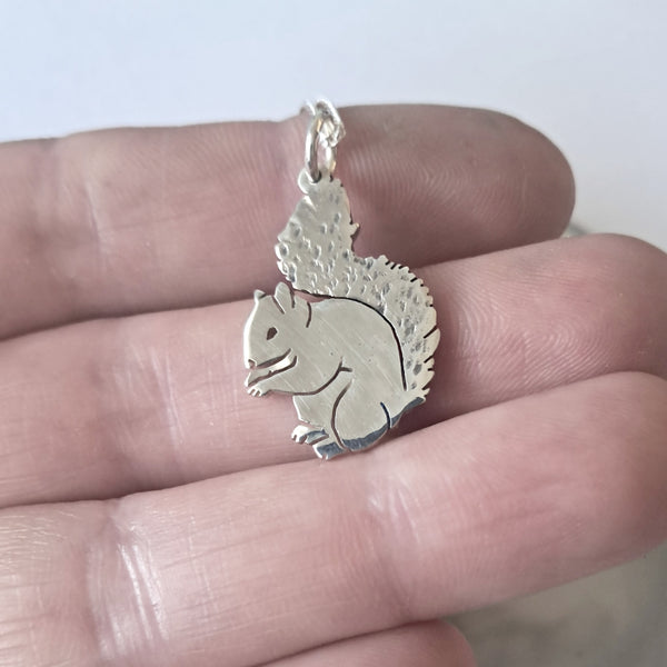 Silver squirrel pendant held between fingers against a neutral background