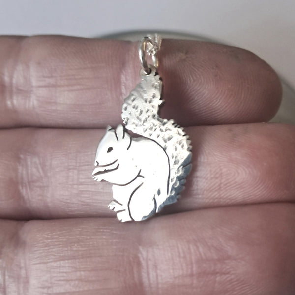 Silver squirrel pendant held between fingers against a neutral background