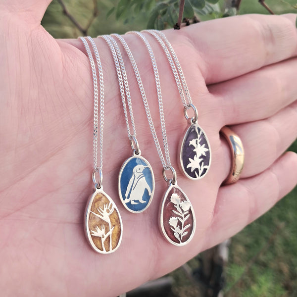 Four silver necklaces with pendant designs held in a hand against a natural background