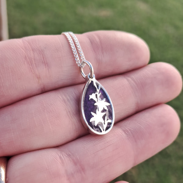 Silver necklace with a pendant held in a hand against a blurred green background