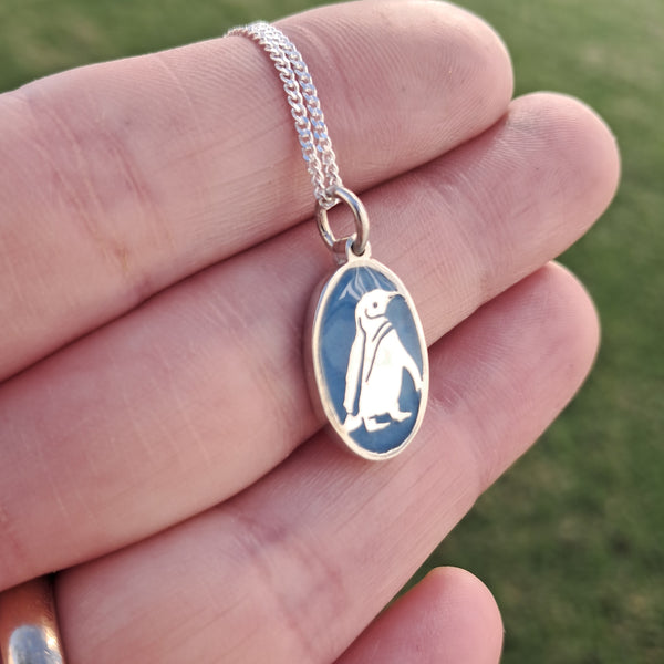 Silver necklace with a penguin pendant held in a hand against a blurred green background