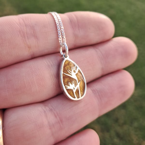 Silver necklace with a pendant featuring a strelitzia flower design held in a hand against a blurred green background