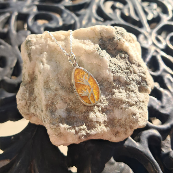 Silver necklace with a yellow pendant on a textured stone surface