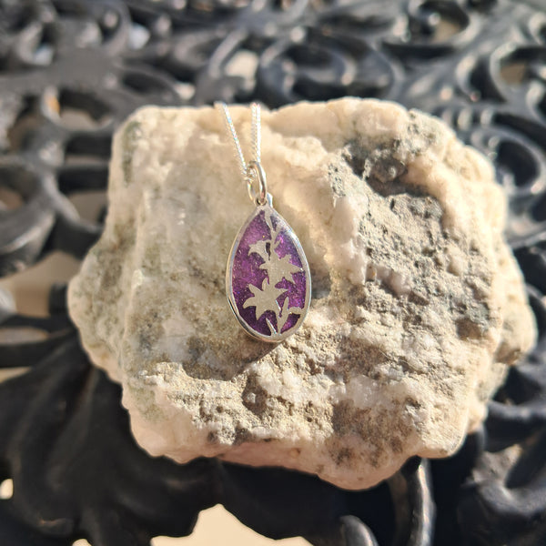 Purple pendant on a silver chain on a rock with intricate metalwork in the background