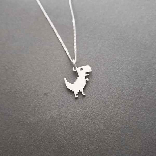 A silver dinosaur pendant necklace on a matching silver chain, displayed against a dark gray textured background.