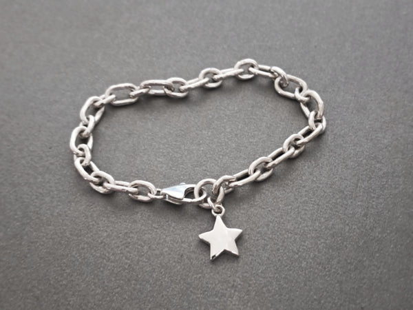 A silver chain bracelet with a small five-pointed star charm, displayed on a textured dark gray background.