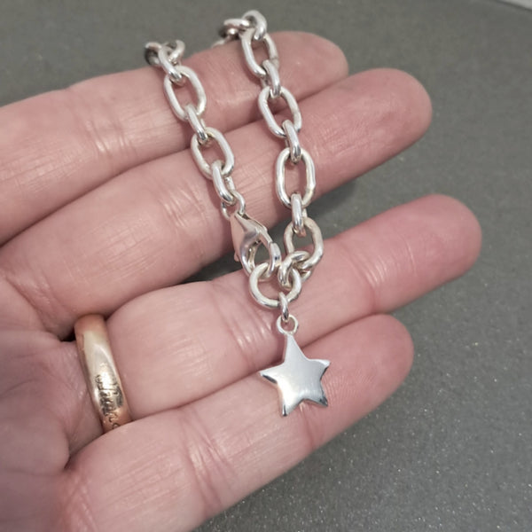 A silver chain bracelet with a star-shaped charm, held in a person's hand. 