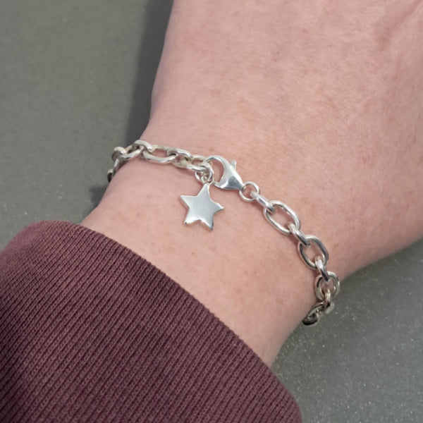 A silver chain bracelet with a small star charm worn on a person's wrist