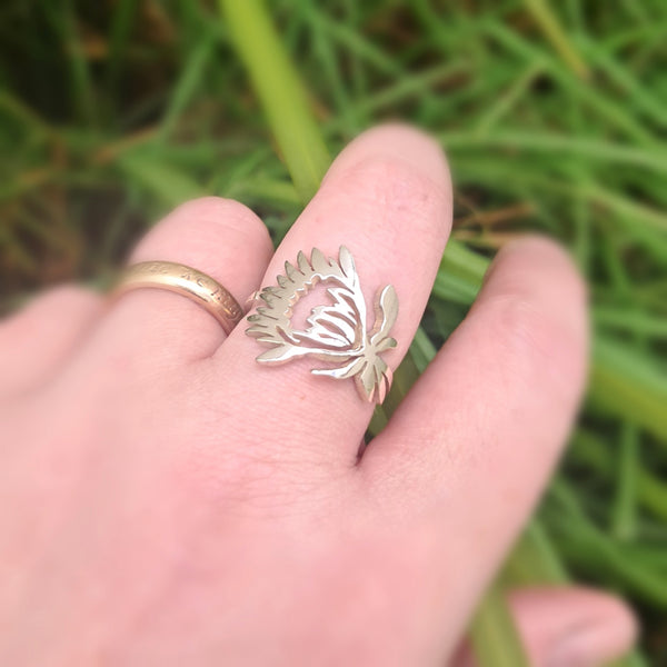 Silver protea flower ring on a finger with a blurred green background